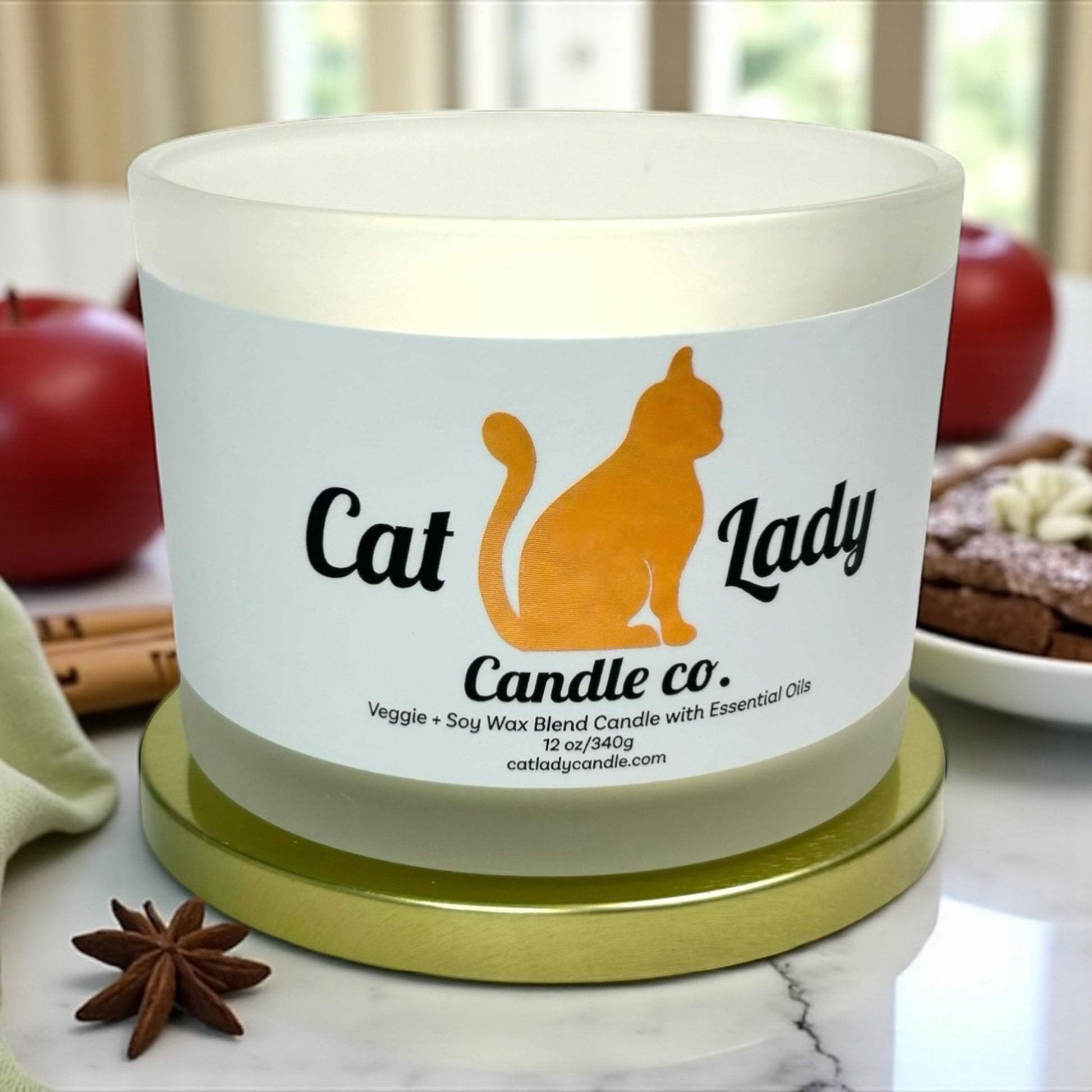 Candle with 'Cat Lady Candle Co.' label on a marble surface with apples, cinnamon sticks and fresh cinnamon toast around it.