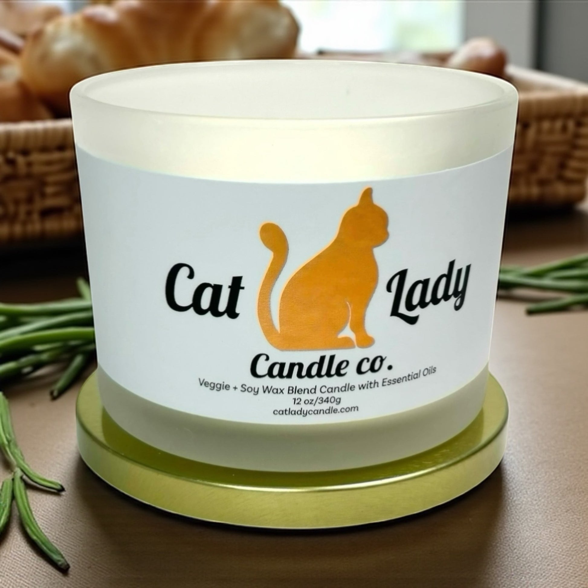 Frosted candle on wooden surface with a label that says Cat Lady Candle Co. Fresh baked bread in the background