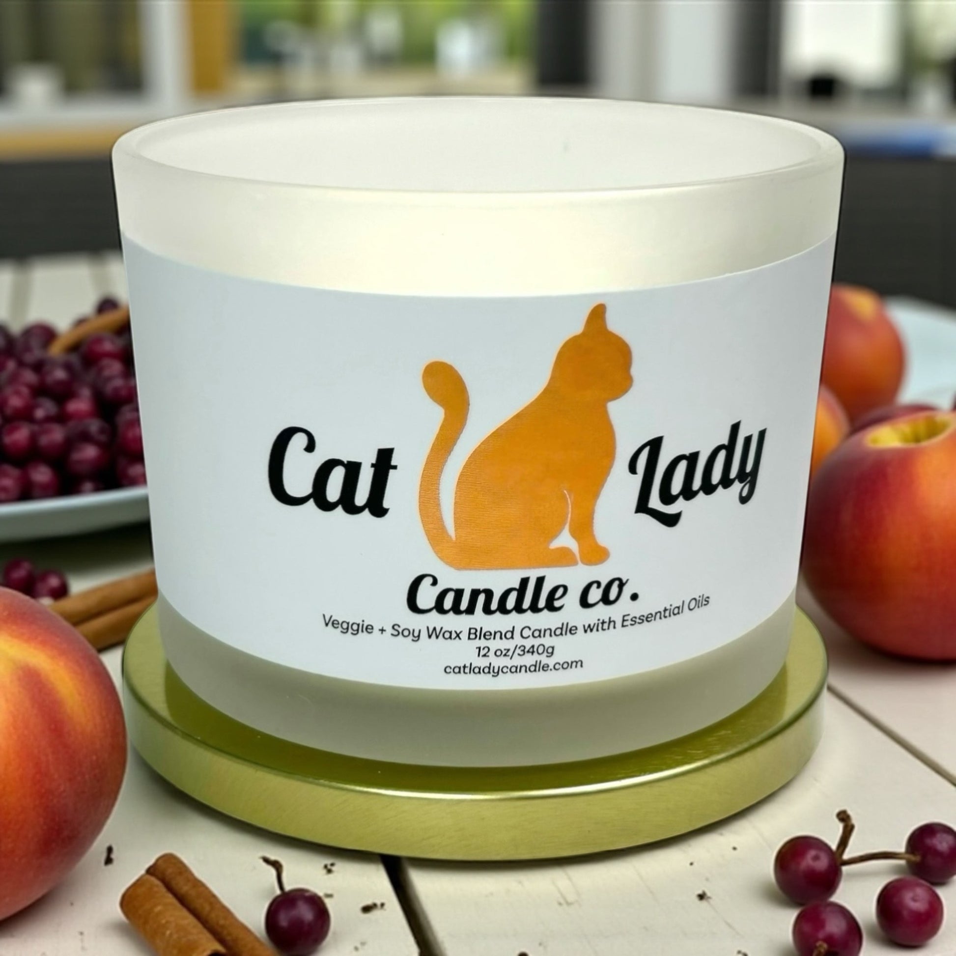 Candle with 'Cat Lady Candle Co.' label on a table with peaches, grapes and cinnamon around it.