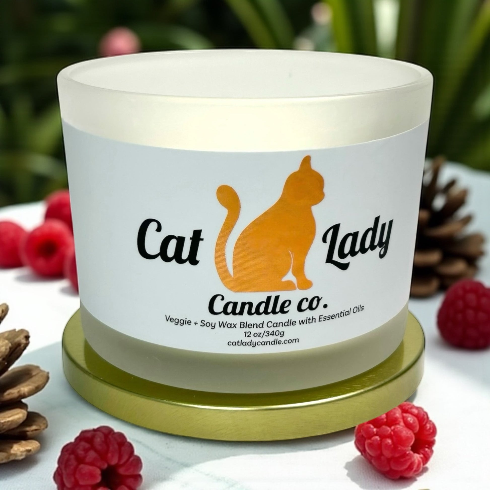 Candle with 'Cat Lady Candle Co.' label surrounded by raspberries and pinecones.