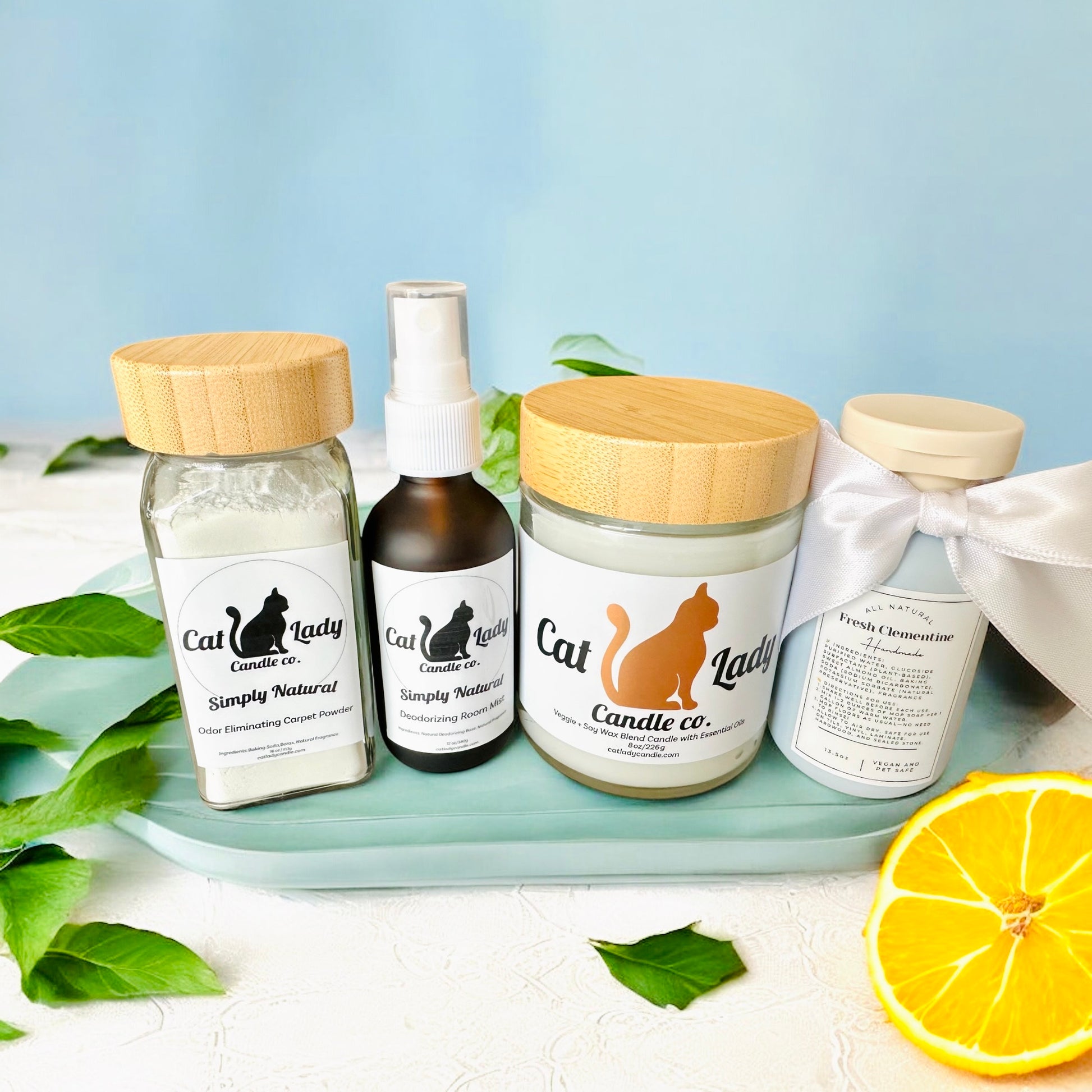 Cat Lady Candle Co cleaning products including a candle, room spray, carpet powder, and concentrated cleaning solution on a tray with a lemon and leaves surrounding them.