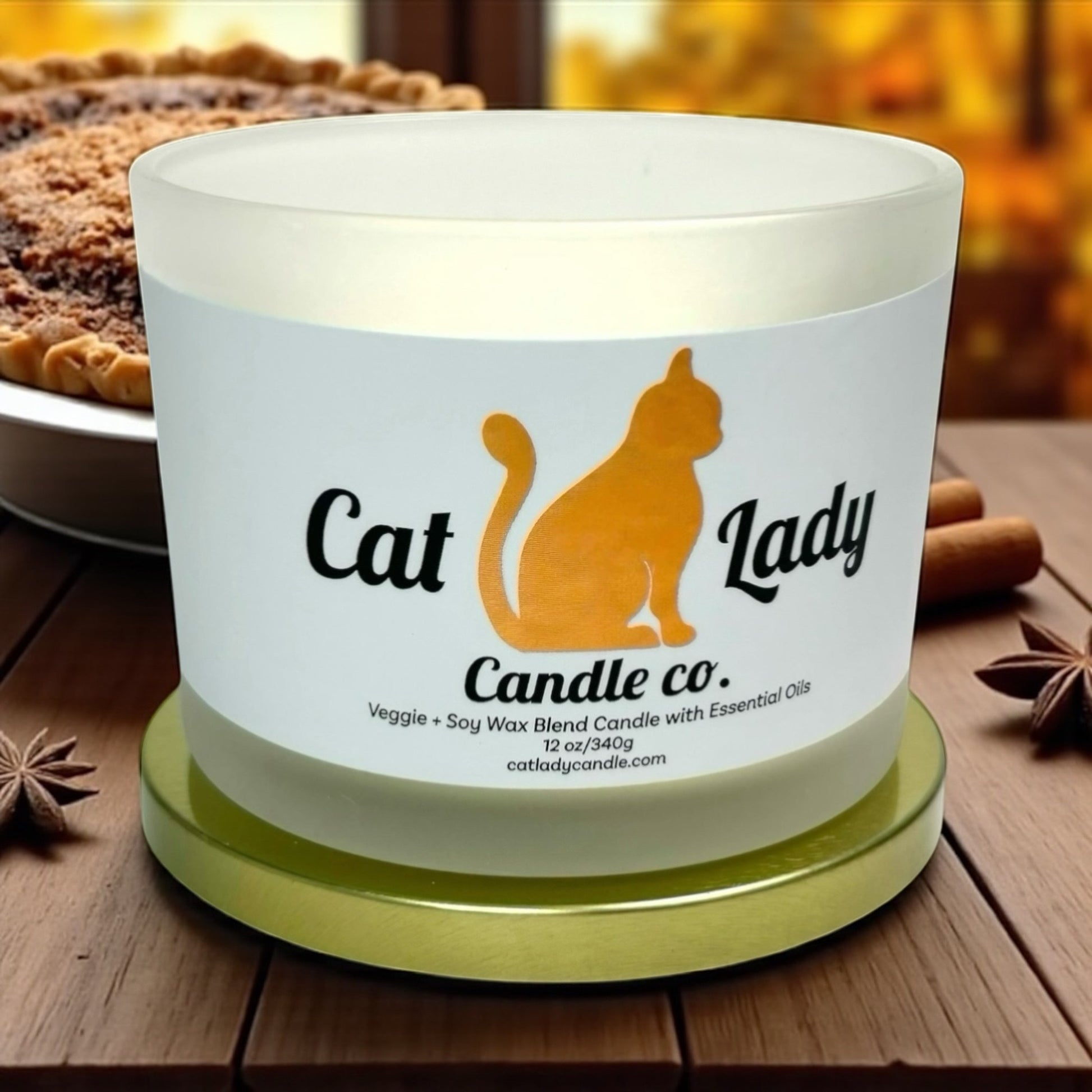 Cat Lady Candle Co. candle on a wooden surface with cinnamon sticks, star anise and a fresh baked sweet potato pie in the background.