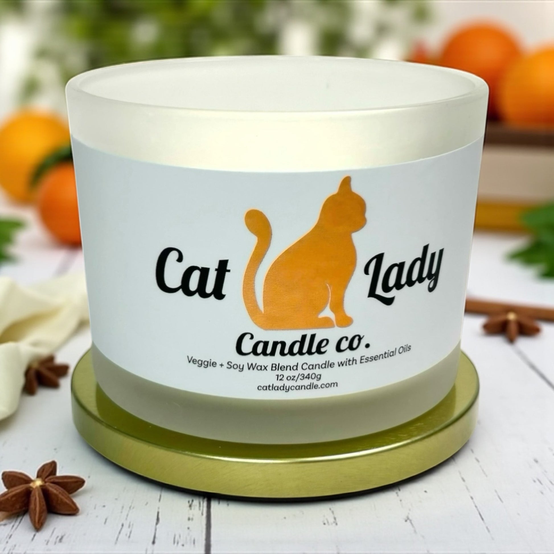 Candle with 'Cat Lady Candle Co.' label on a white surface with decorative star anise, cinnamon and tangerines in background.